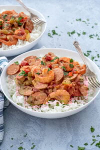 A large white bowl with a large scoop of gumbo on top of a bed of white rice with a fork.