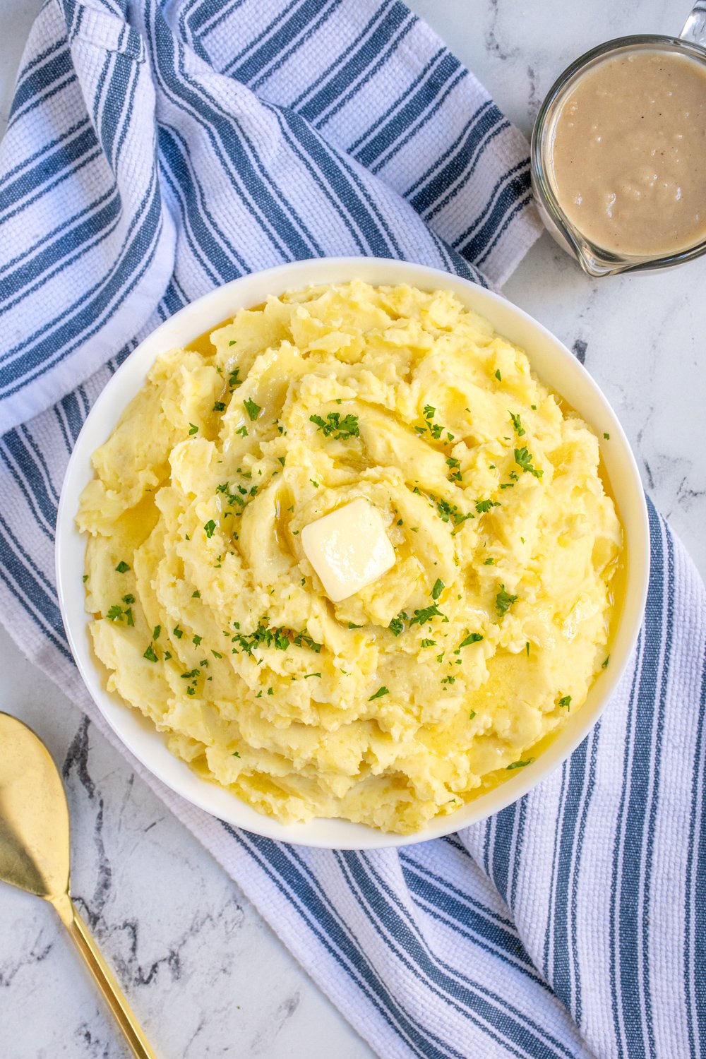 Overhead view of a large bowl of classic mashed potatoes top with a slab of butter and garnished with fresh parsley.