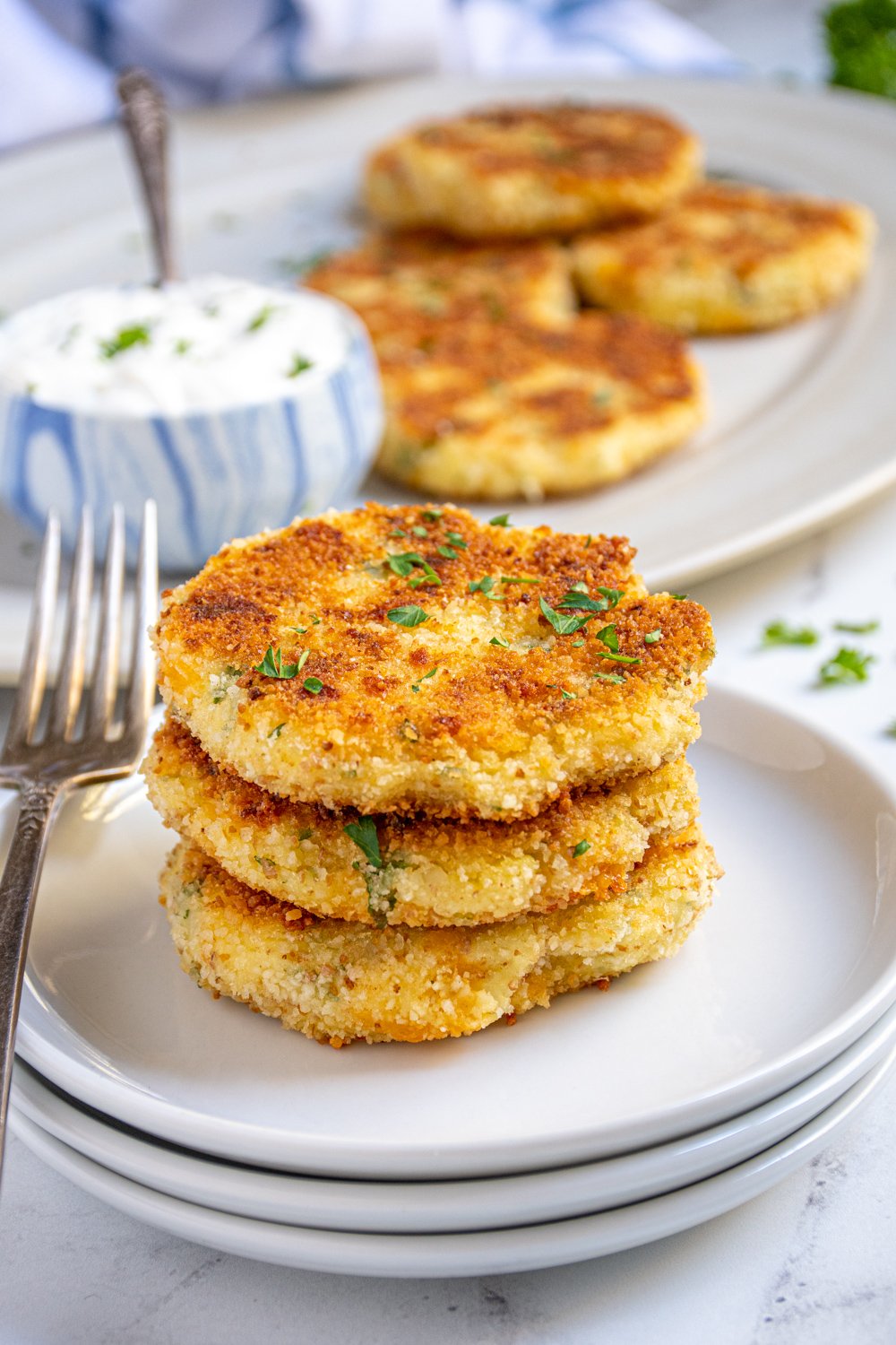 Three golden brown mashed potato cakes staked on a plate next to a fork.