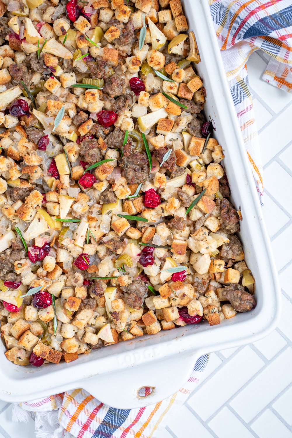 Overhead photo of an angled white dish with stuffing filled with sausage, cranberries, and apples.