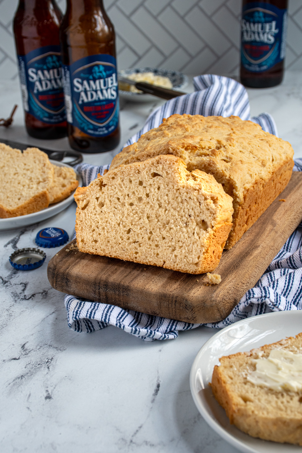 a slice and loaf of beer bread on a cutting board surrounded by slices of bread and a few beer bottles.