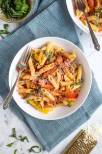 Overhead view of a white bowl with a fork filled with sausage and pepper penne pasta, garnished with parmesan cheese.