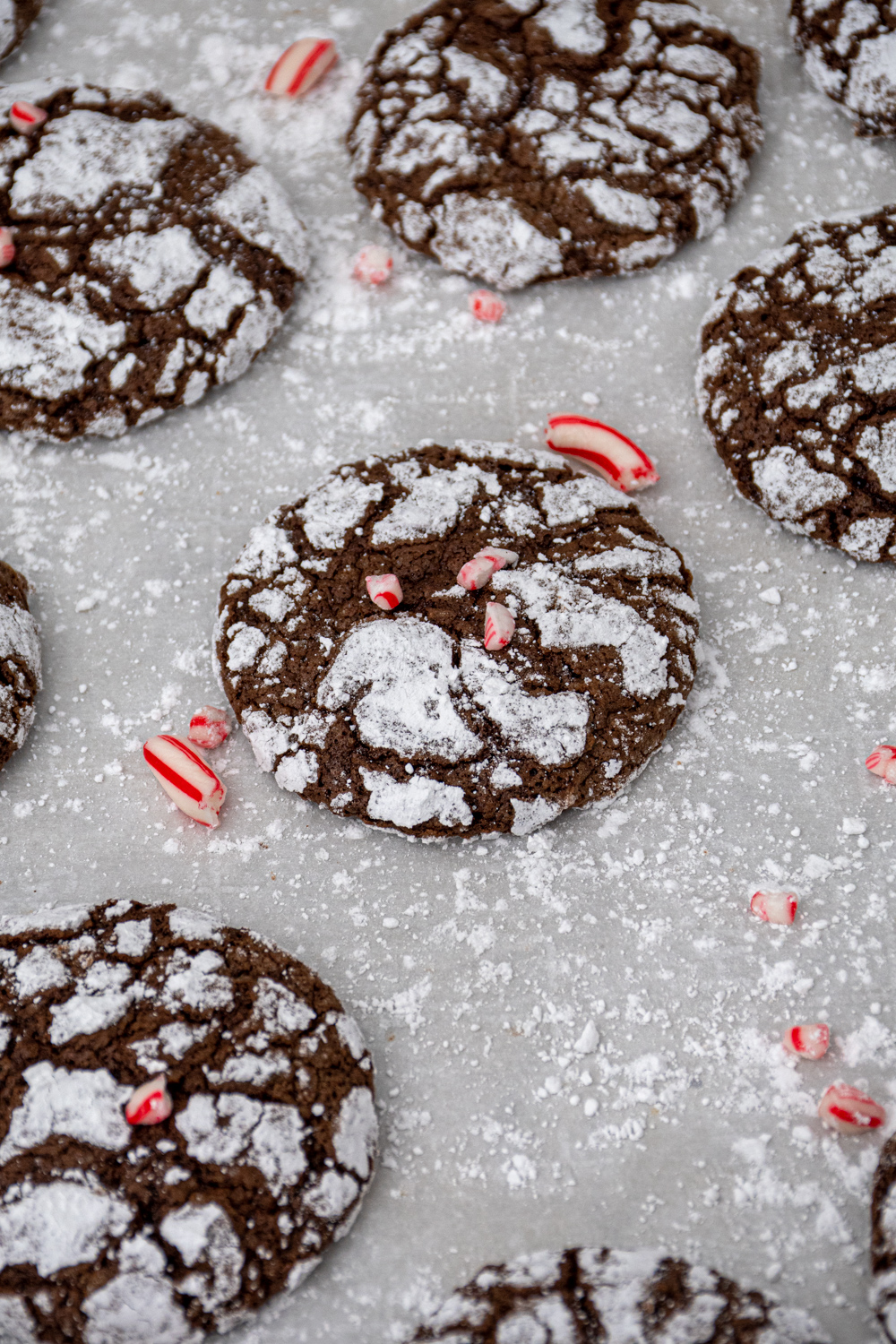 Close up of a chocolate peppermint crinkle cookie sitting on parchment paper garnished with crushed candy canes.