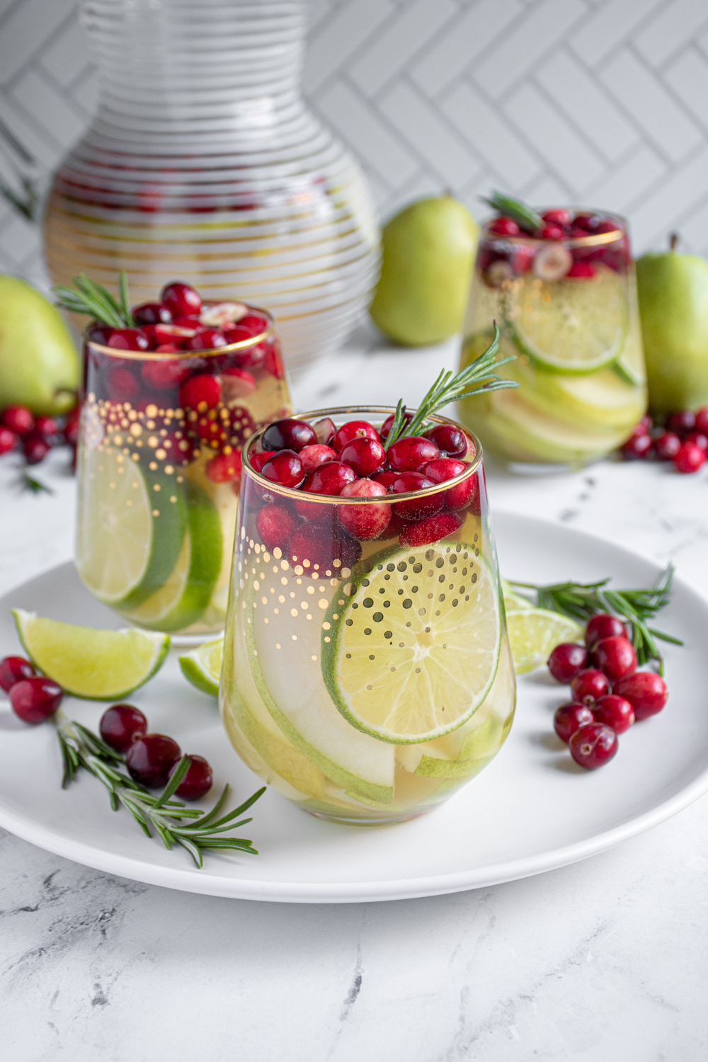 Stemless glasses with white winter sangria filled with pears, limes, cranberries, and topped off with fresh rosemary.