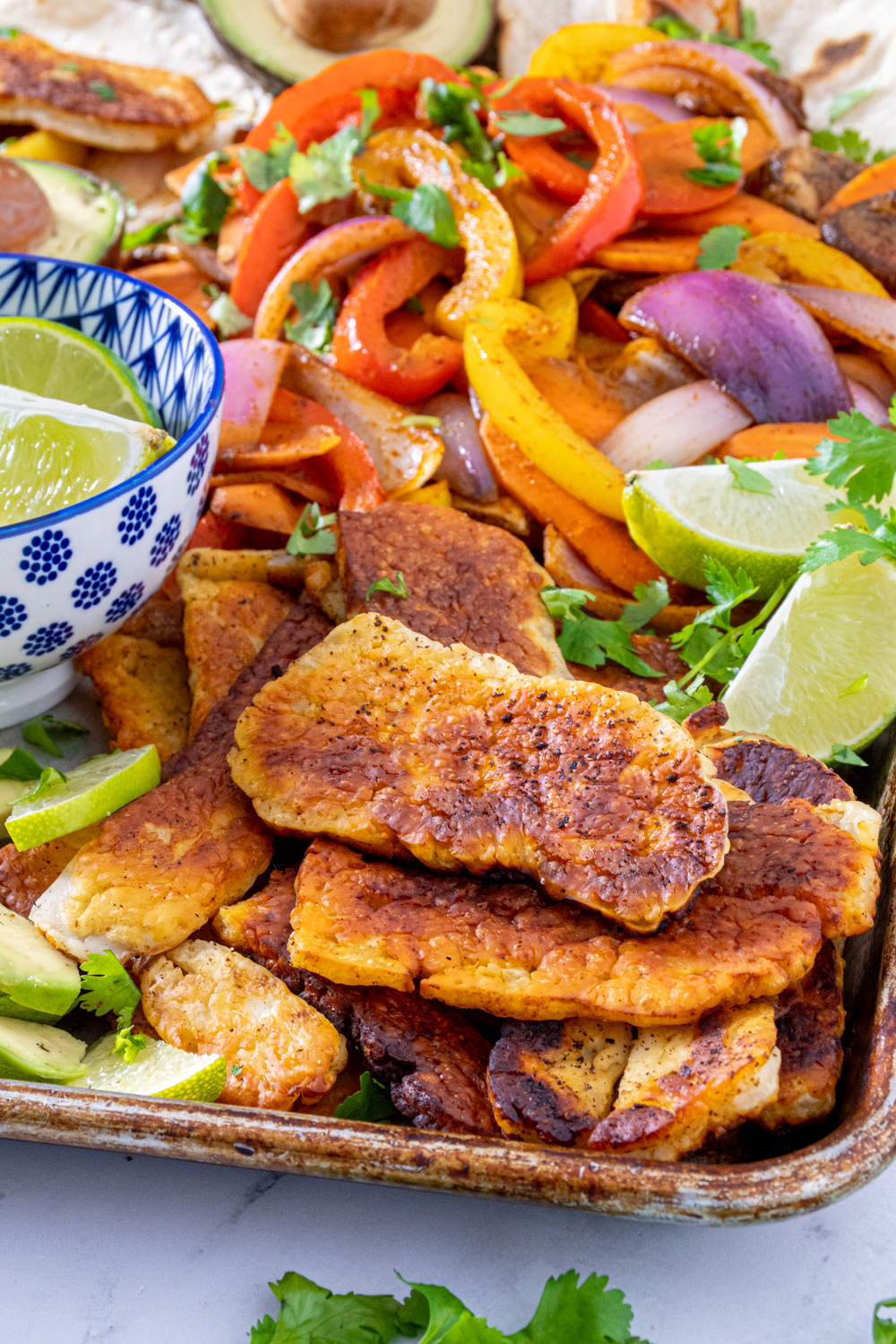 Close up of golden brown cooked halloumi on a tray next to fajita veggies and lime wedges.