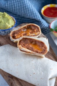 Close up of refried bean burrito cut open showing the insides on a cutting board.