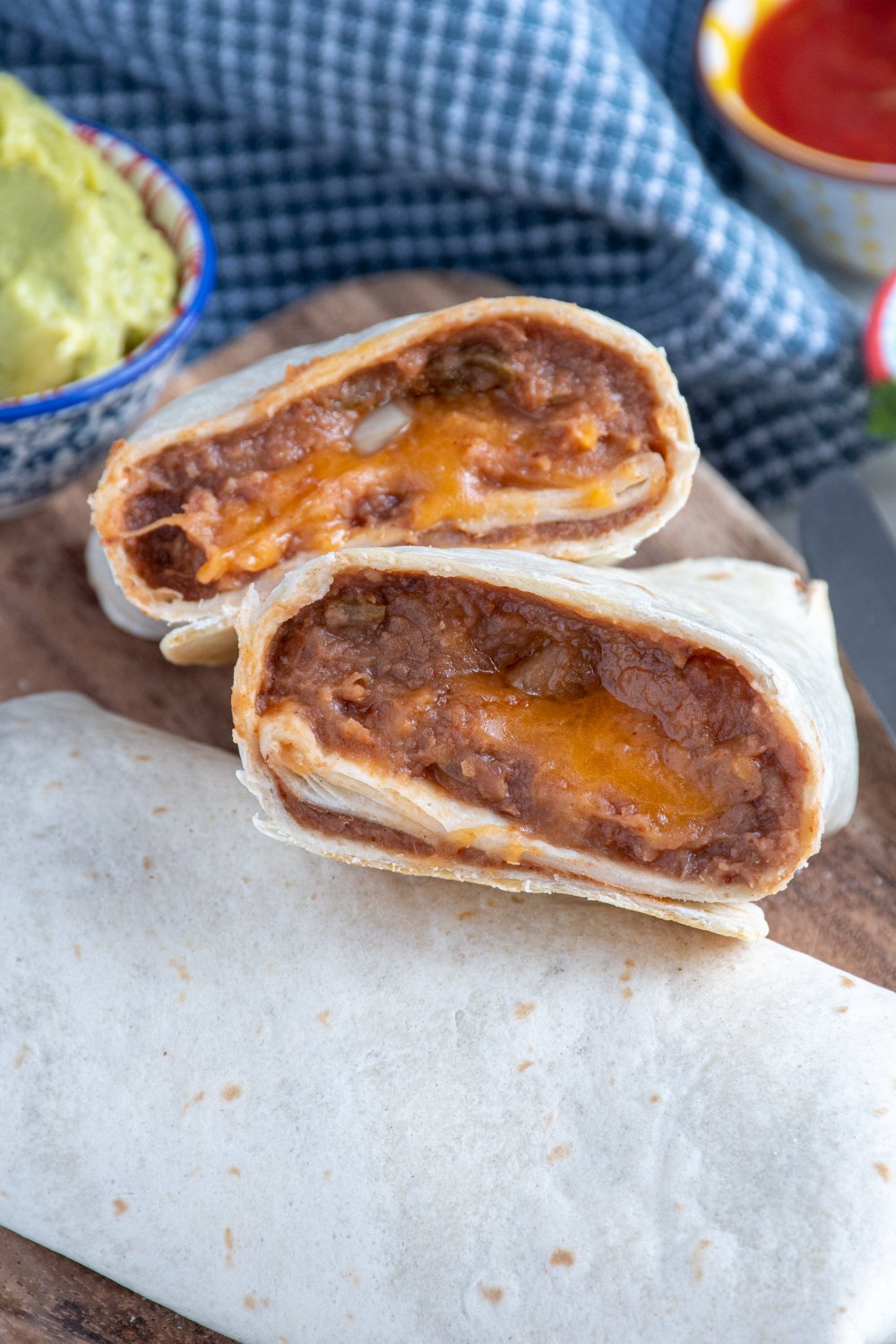 Refried bean burrito cut in half showing the cheesy insides on a cutting board.