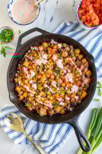 Cast iron skillet holding ground turkey and sweet potato skillet with black bean garnished with diced tomatoes, sliced green onions, and a drizzle of sauce.