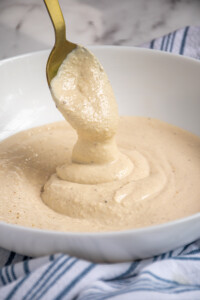 Greek Yogurt Caesar Dressing drizzling off of a spoon into a bowl of dressing.
