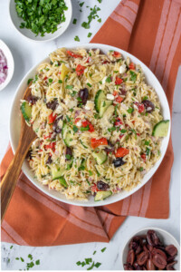 A white bowl filled with Mediterranean Orzo Salad with a wooden spoon for serving and garnished with fresh parsley.