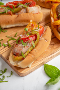 An Italian Sausage with peppers and onions in a bun topped with fresh basil and grated parmesan cheese.