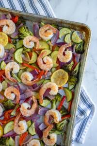 Close up of the corner of sheet pan shrimp and veggies with colorful vegetables and plump juicy shrimp.