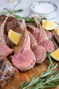 A few pieces of cut grilled rack of lamb on a wooden cutting board showing off the rosy interior color of the grilled lamb meat.