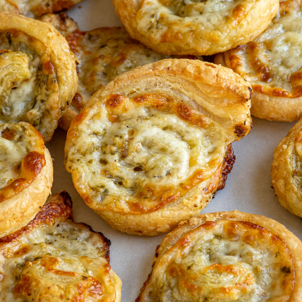 Pesto pinwheels on a platter with the one in the center of focus showing off the melty cheese and pesto center.