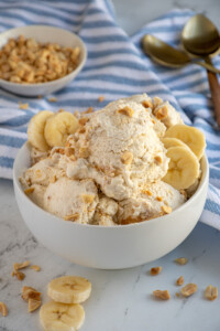 A bowl filled with cottage cheese ice cream garnished with crushed peanuts and banana slices.