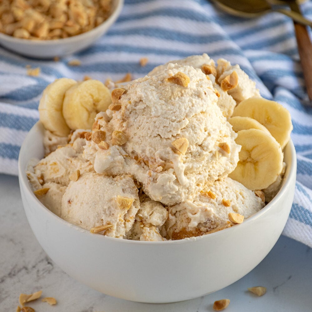 A bowl filled with cottage cheese ice cream garnished with crushed peanuts and banana slices.