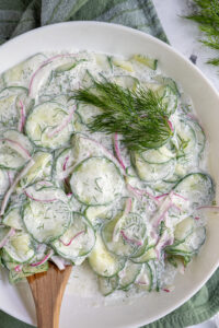A white bowl filled with creamy cucumber salad with dill for garnish.