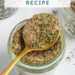 Pinterest Pin with text overlay "Greek Seasoning Recipe", image of a jar with a resting spoon full of greek seasoning.