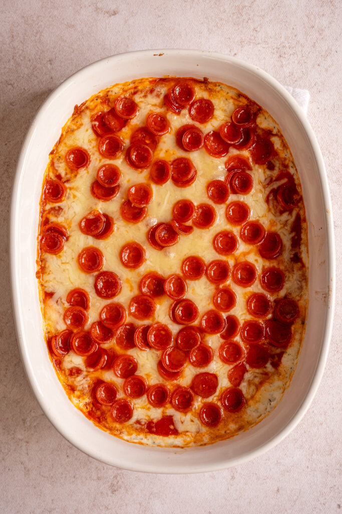 A white casserole dish with baked cottage cheese pizza dip with mini pepperonis.