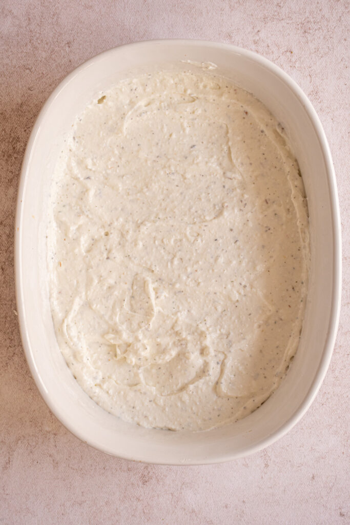 Blended cottage cheese with italian seasoning spread out into a casserole dish.