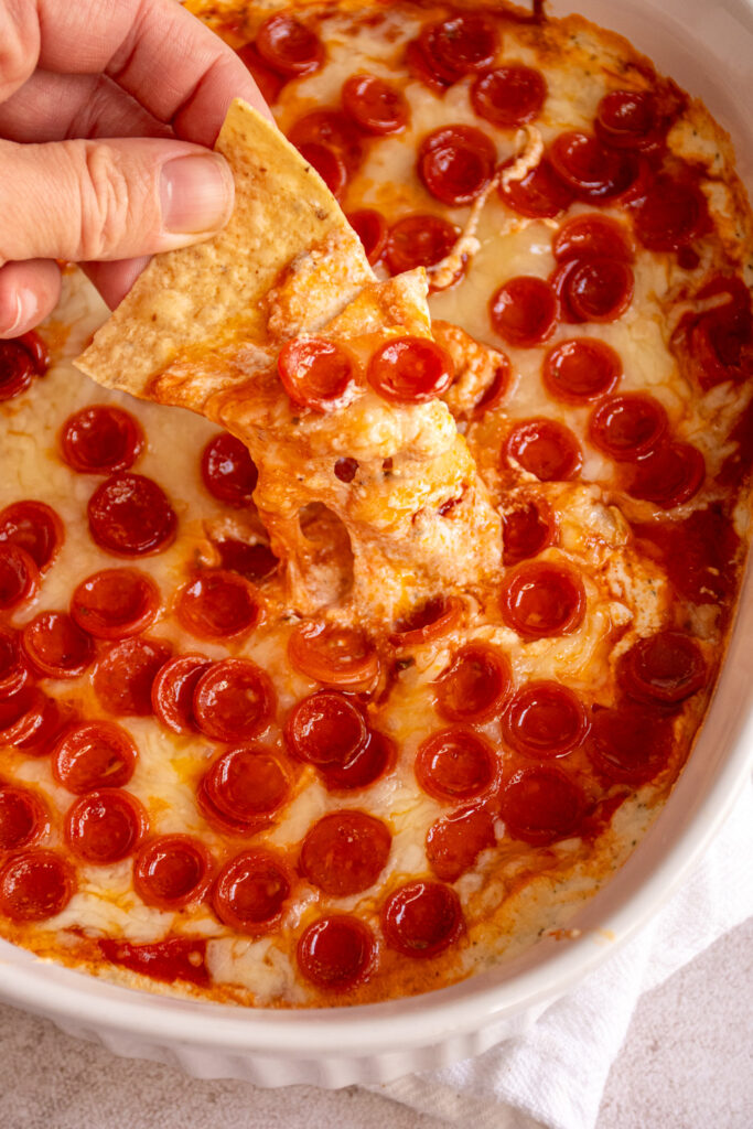 Dipping a tortilla chip in hot cottage cheese pizza dip with the cheese pulling after the chip.