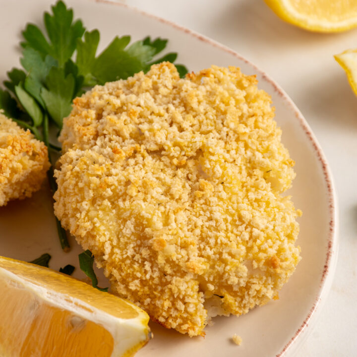 Plates with pieces of crispy baked breaded cod with lemons and fresh parsley.