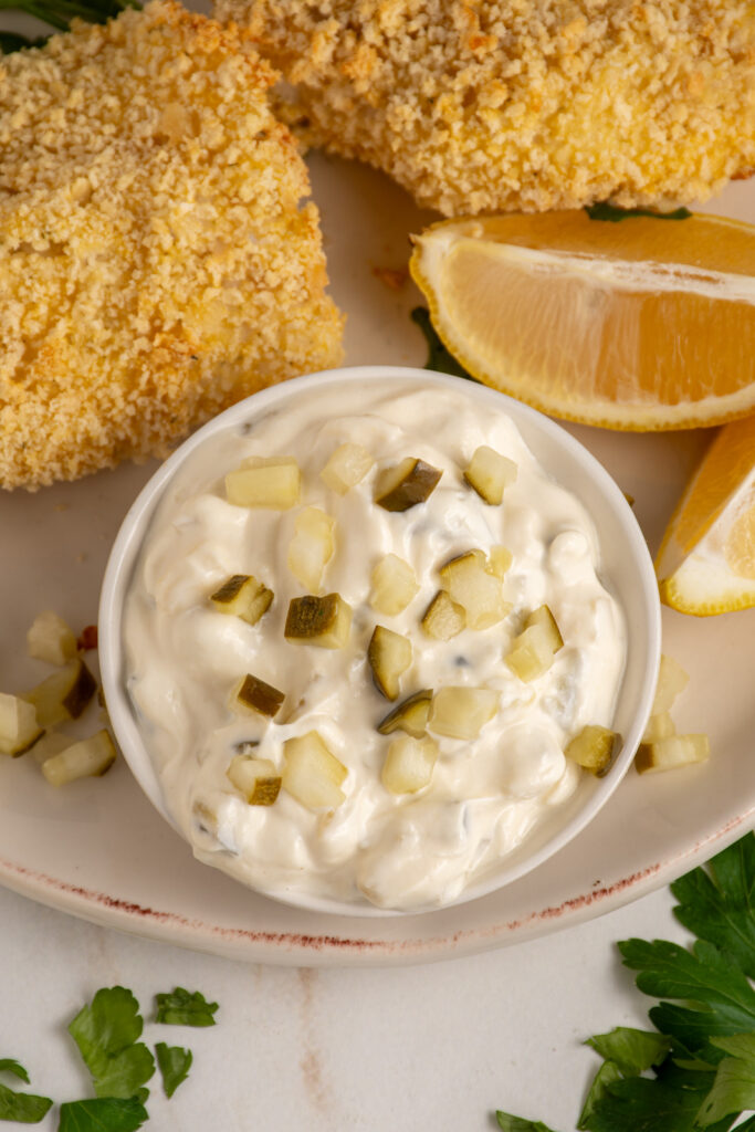 A small bowl with tartar sauce made with greek yogurt garnished with chopped pickles.