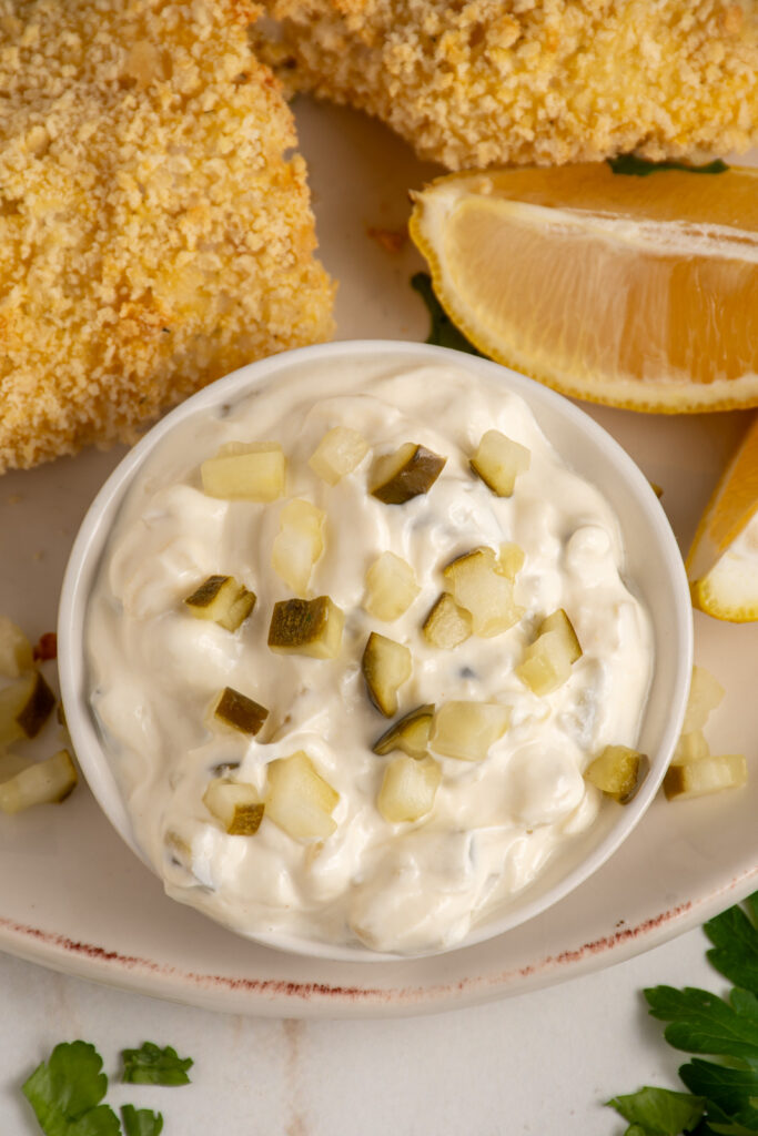 A small bowl with tartar sauce made with greek yogurt garnished with chopped pickles.