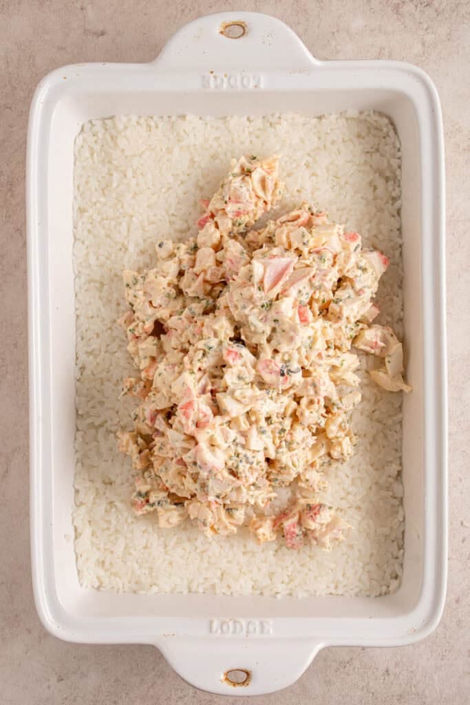 Adding crab mixture to the top of the rice in the casserole dish.