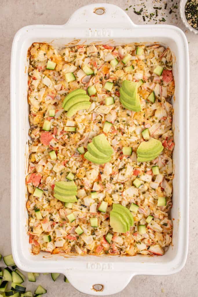 A casserole dish with shrimp and crab sushi bake garnished with avocados.