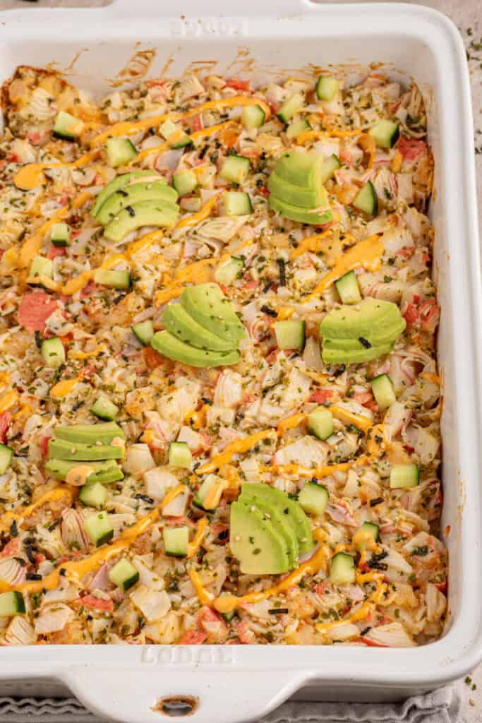 A casserole dish with shrimp and crab sushi bake garnished with avocados.