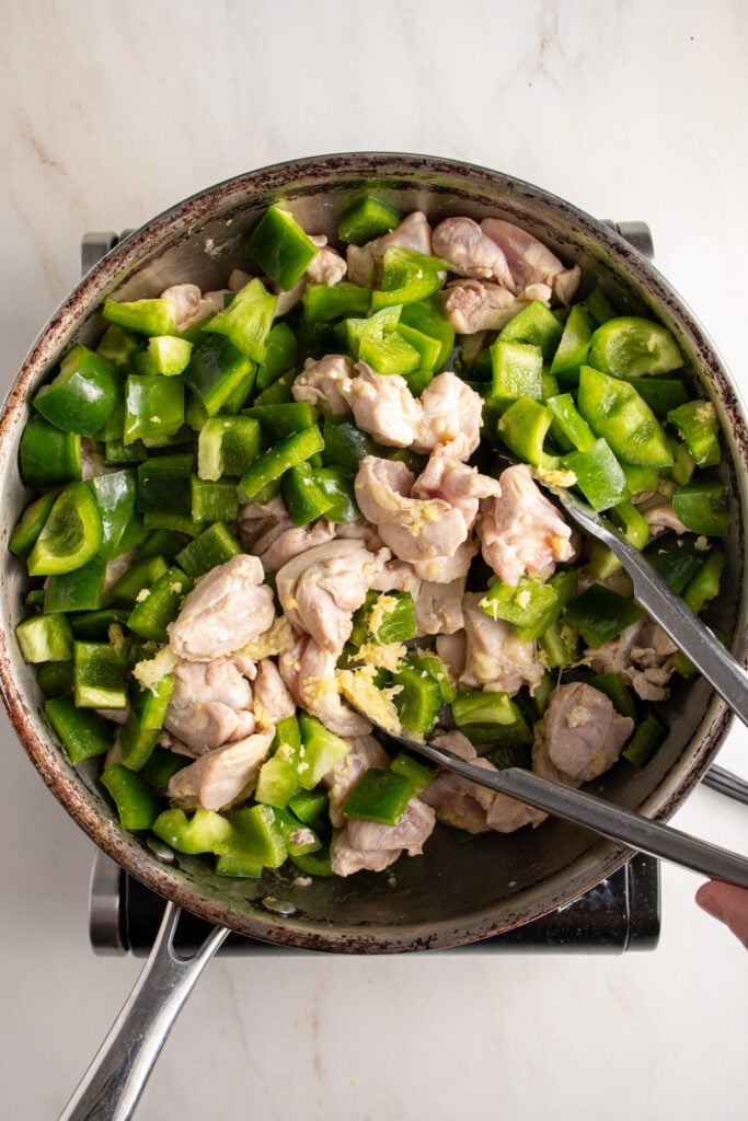 Cooking chicken and green pepper in a skillet.