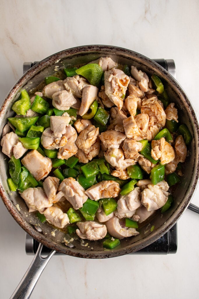 Adding sauce to a skillet of chicken and pepper.