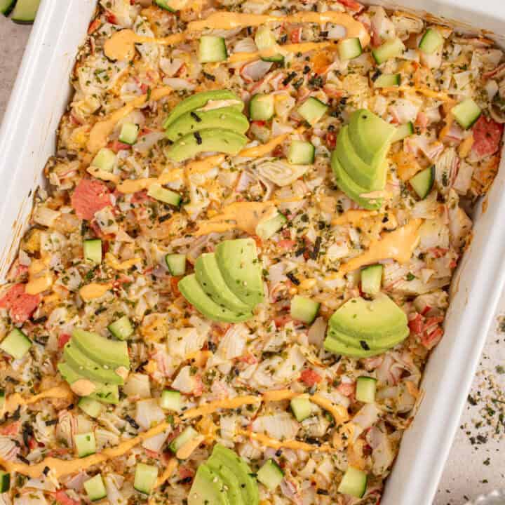 A casserole dish with shrimp and crab sushi bake garnished with avocados.