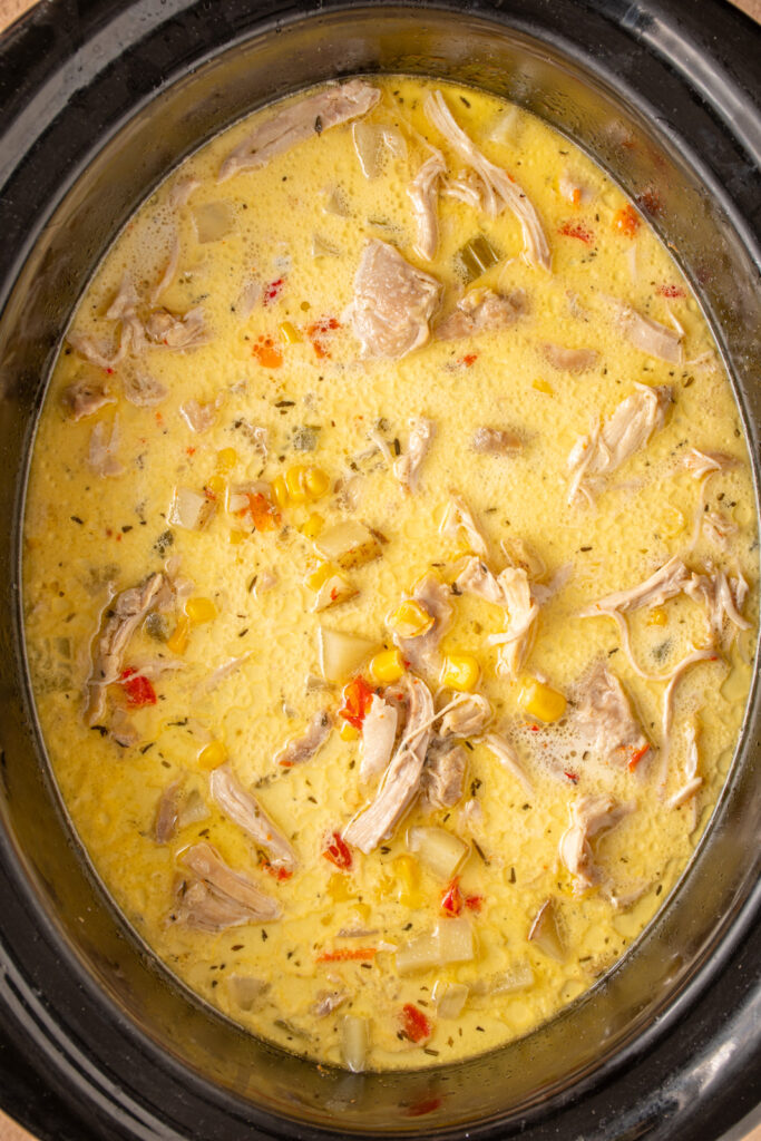 A black crockpot with chicken and corn chowder.