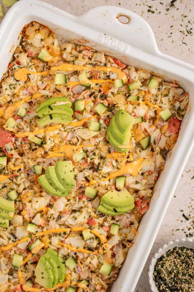 A casserole dish with shrimp and crab sushi bake garnished with avocados.