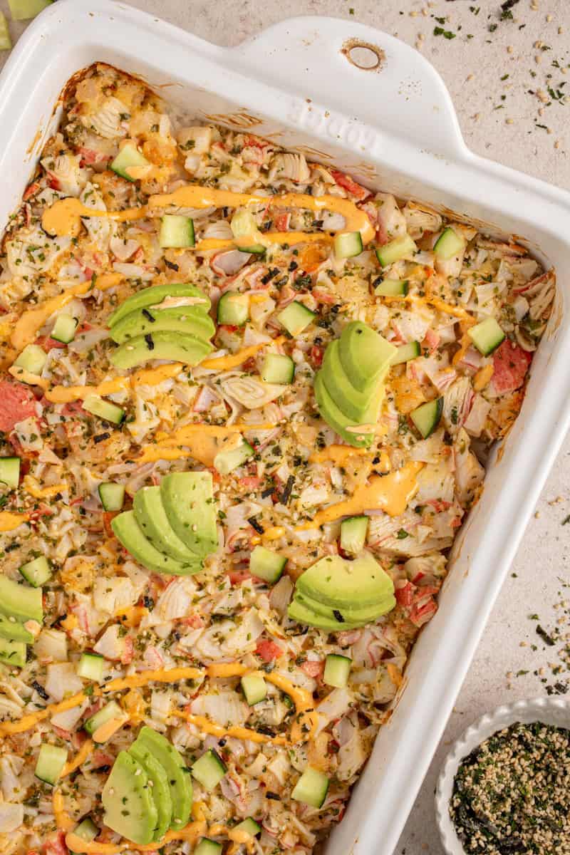 A casserole dish with shrimp and crab sushi bake garnished with avocados.