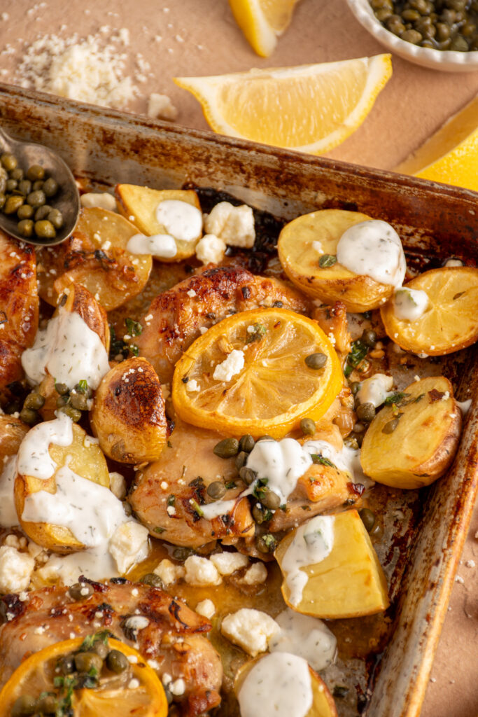 Close up of balsamic chicken thigh on a sheet pan with potatoes and lemons.