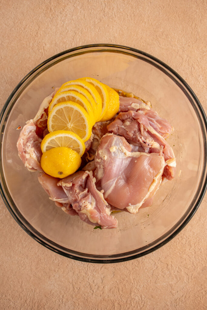 Raw chicken and lemon slices in a bowl.