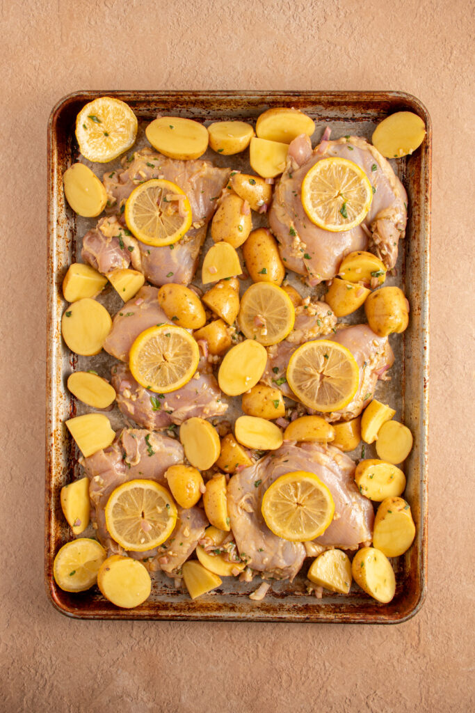 A sheet pan ready to go into the oven with chicken thighs, potatoes, and lemons.