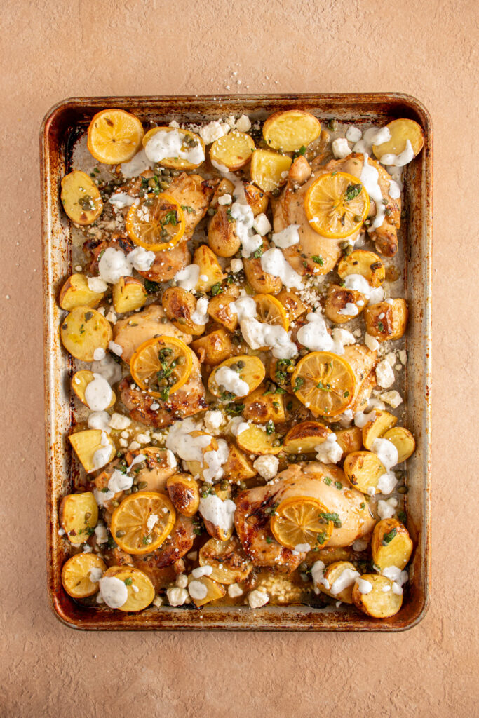 A sheet pan with balsamic chicken thighs, lemon, potatoes, and tzatziki.