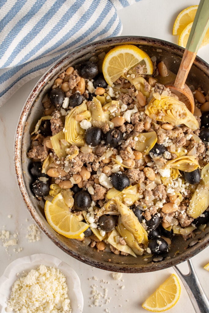 A skillet with ground turkey, black olives, beans, artichoke hearts, and feta cheese.