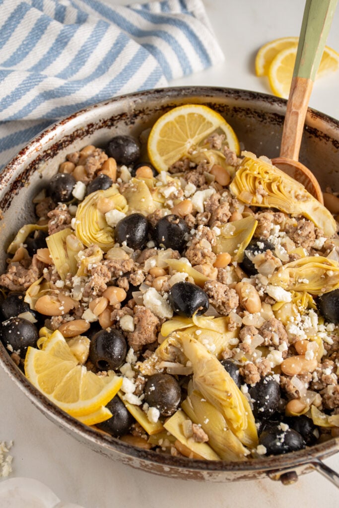 A skillet with ground turkey, black olives, beans, artichoke hearts, and feta cheese.