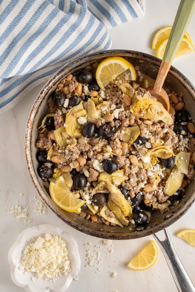 A skillet with ground turkey, black olives, beans, artichoke hearts, and feta cheese.