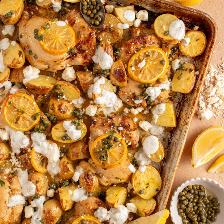 A sheet pan with balsamic chicken thighs, lemon, potatoes, and tzatziki.