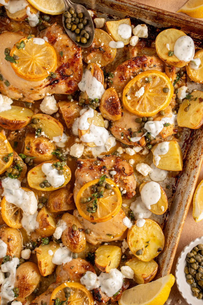 A sheet pan with balsamic chicken thighs, lemon, potatoes, and tzatziki.