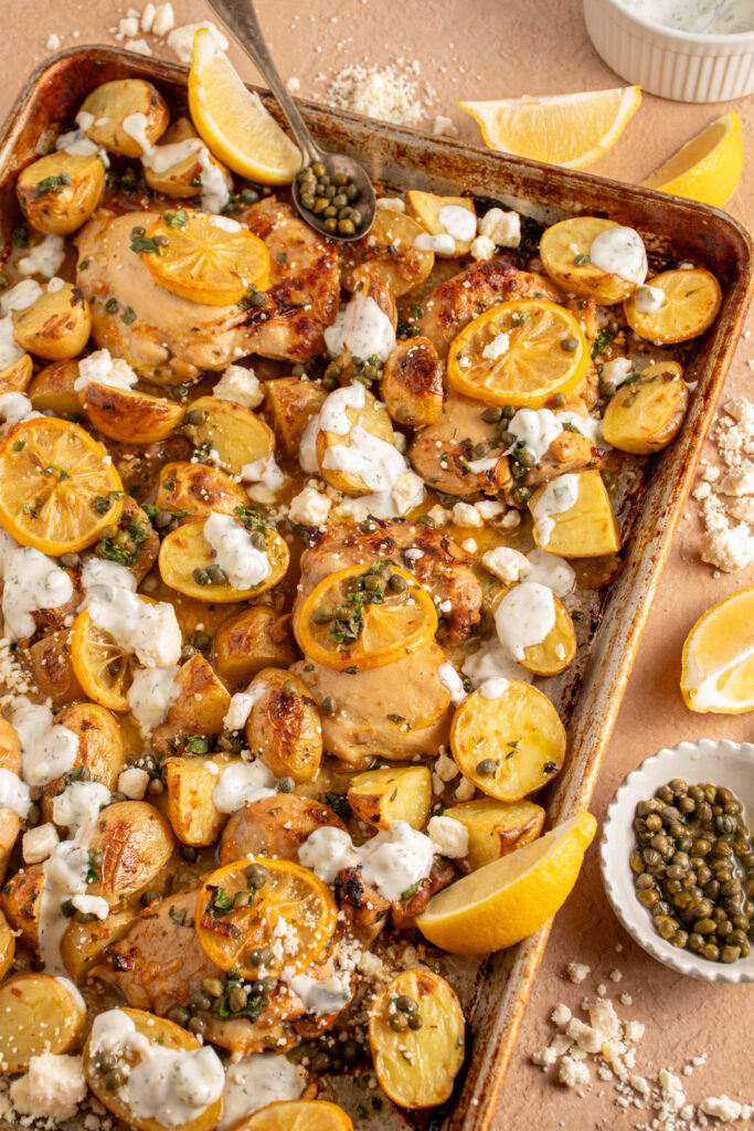 A sheet pan with balsamic chicken thighs, lemon, potatoes, and tzatziki.