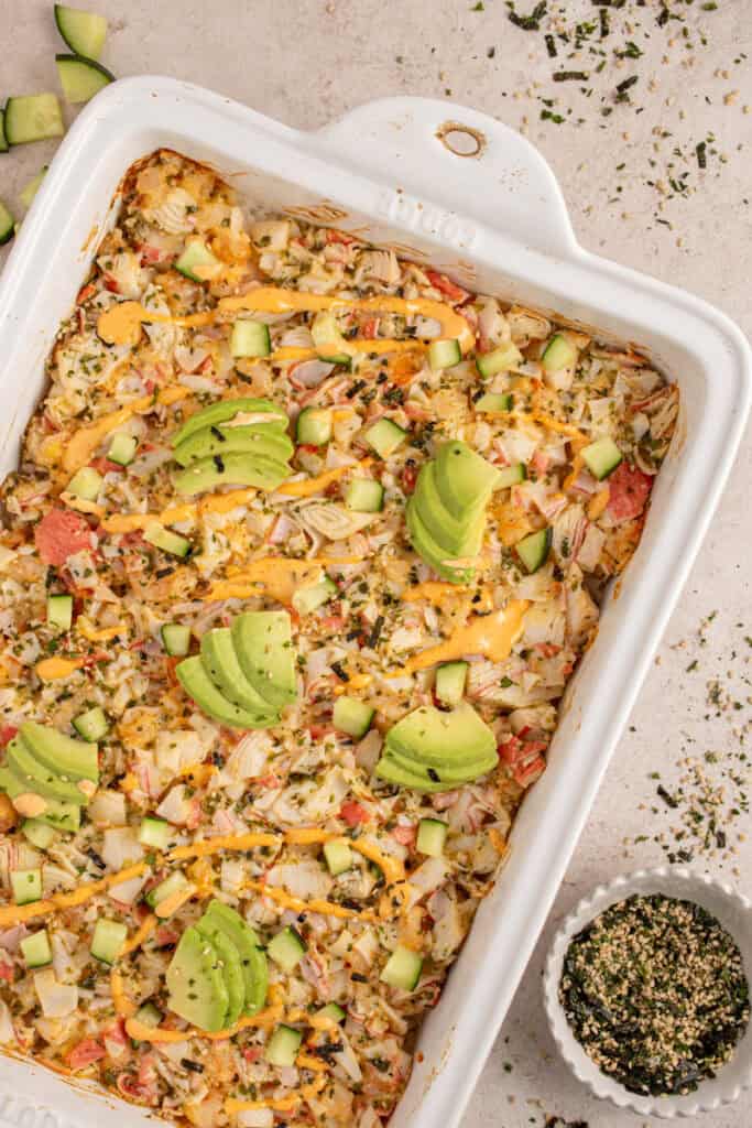 A casserole dish with shrimp and crab sushi bake garnished with avocados.