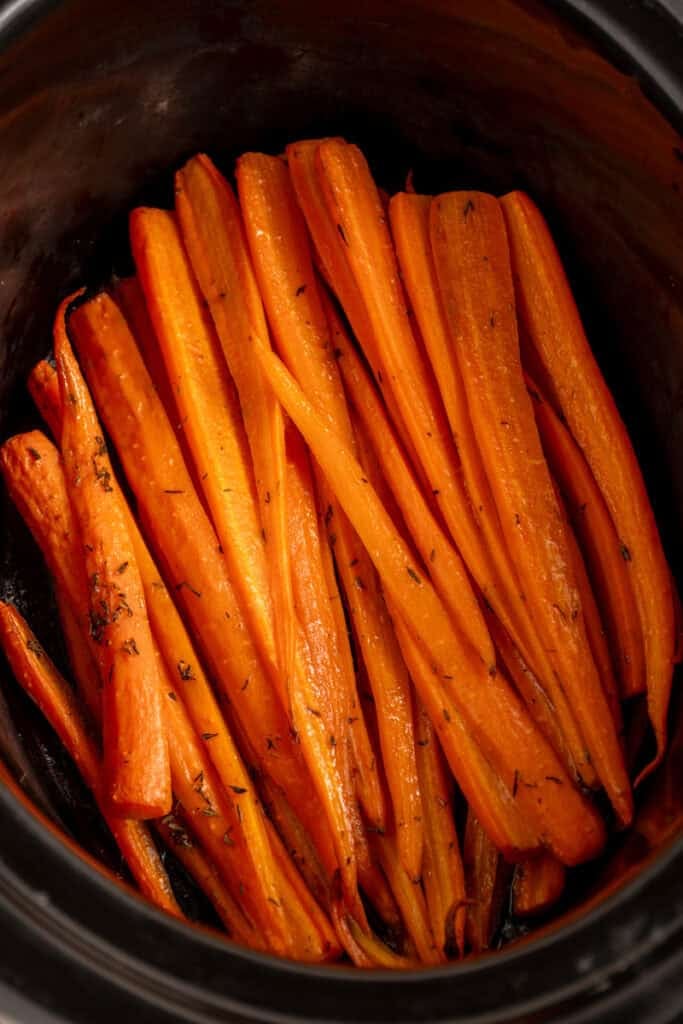 A black crockpot with cooked carrots.