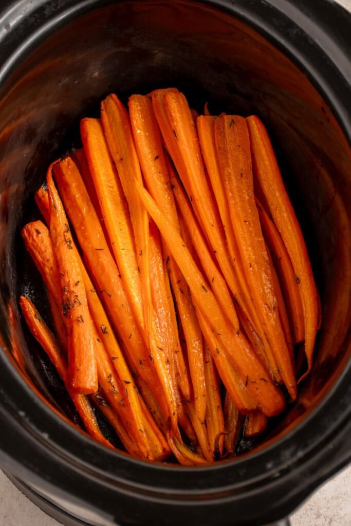 A black crockpot with cooked carrots.